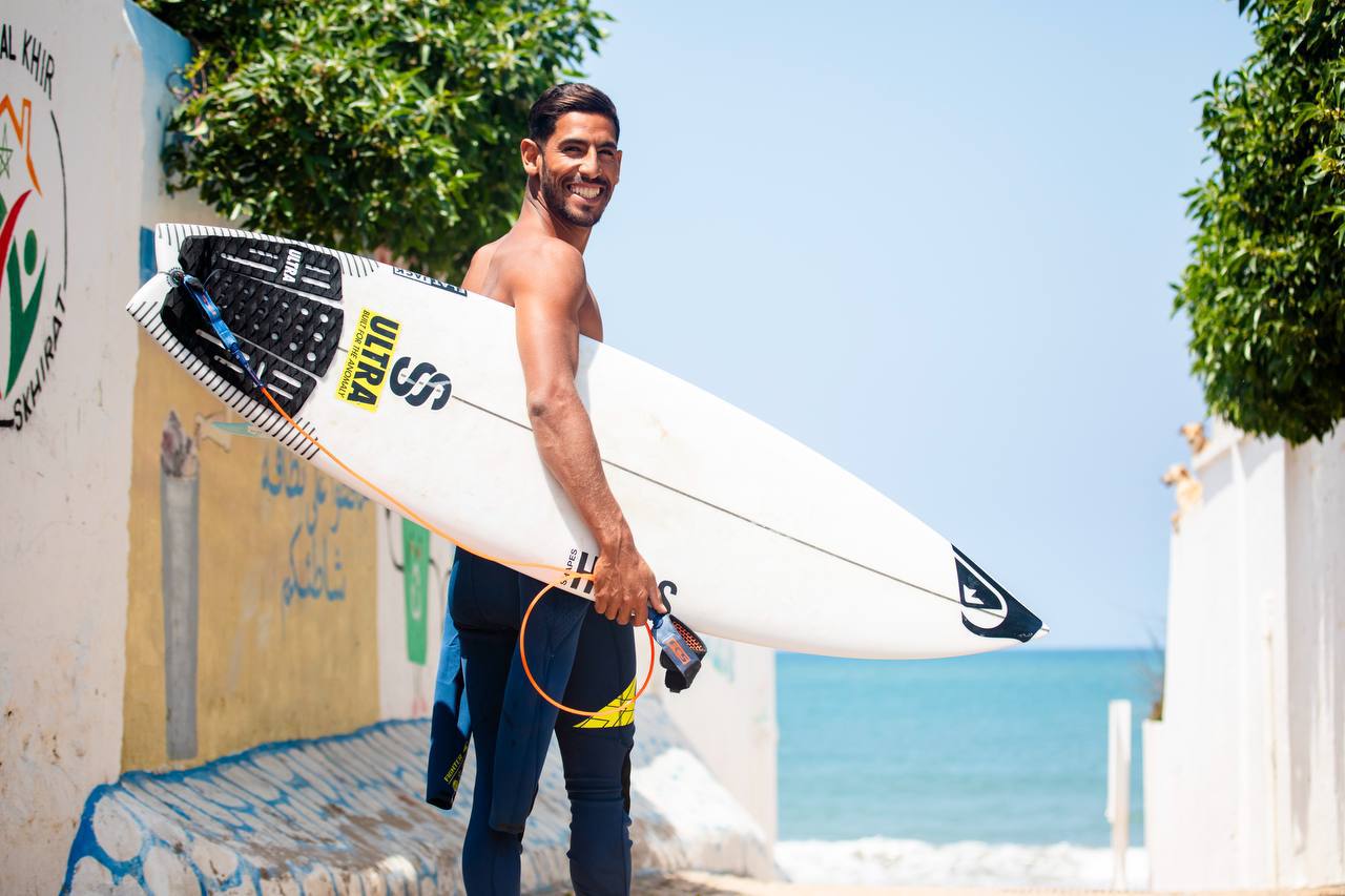Hamza El Bahraoui souriant avec une planche près de l’océan à Taghazout