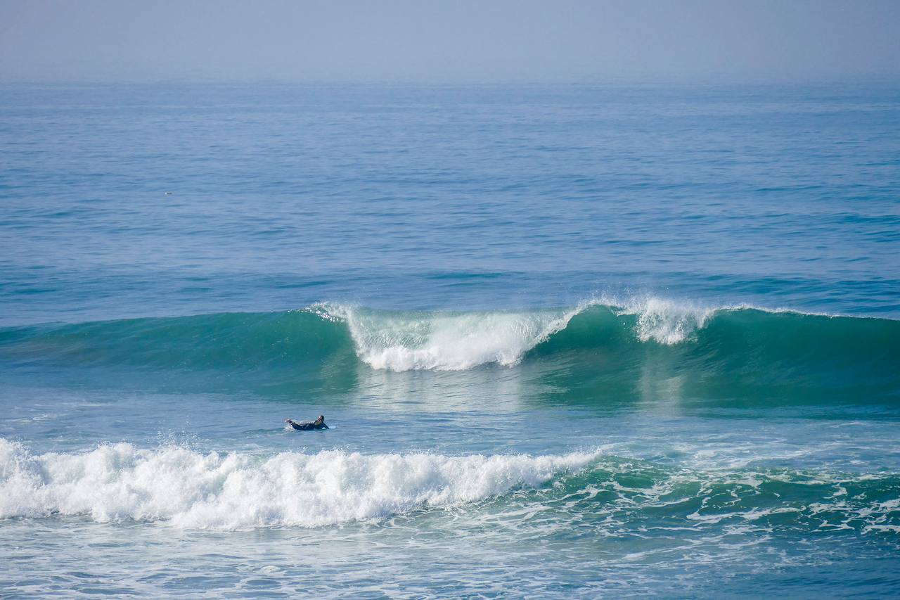Lone surfer paddling behind clean turquoise-green waves in Morocco