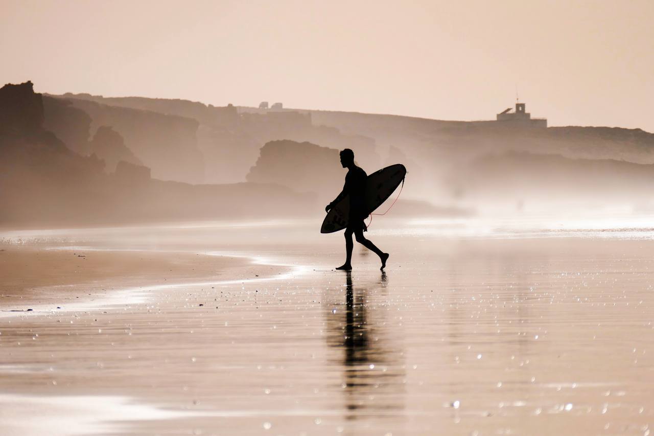 Surfer walking across wet sand at Tamri in Morocco